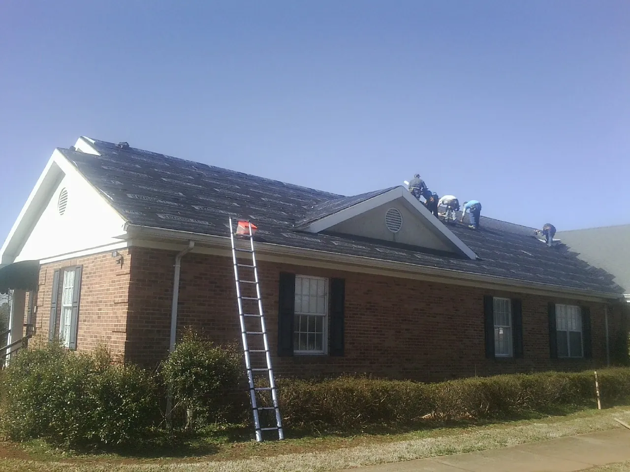 Crew tearing shingles off a brick ranch roof with a ladder set — Metal Roof Repair work by our crew in Bliss