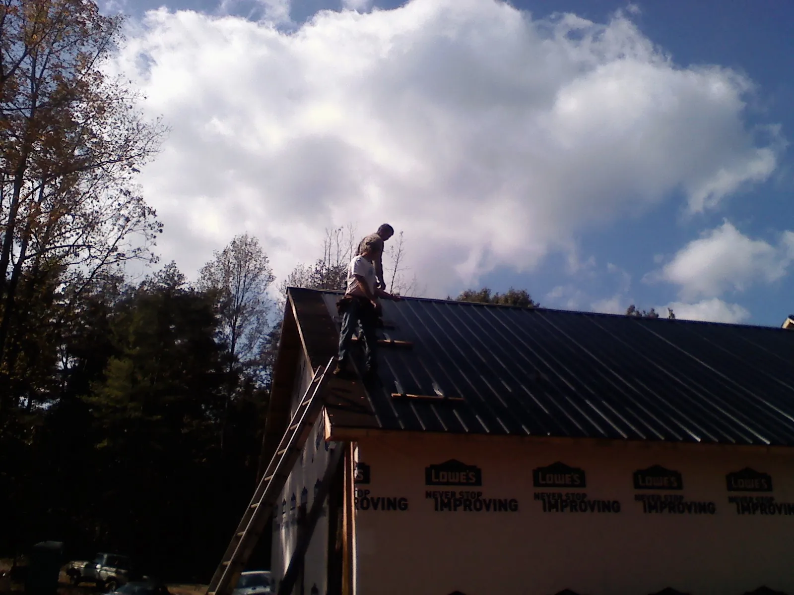 Roofer fastening dark metal panels high against a cloudy sky, from a Roof Inspection job in Bliss